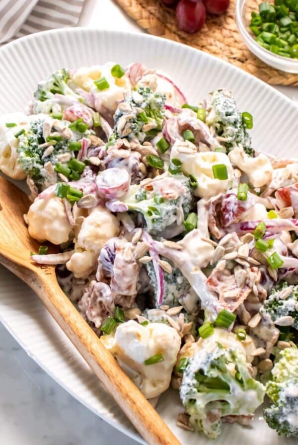 A platter of healthy broccoli and cauliflower salad with a wooden spoon to the side.