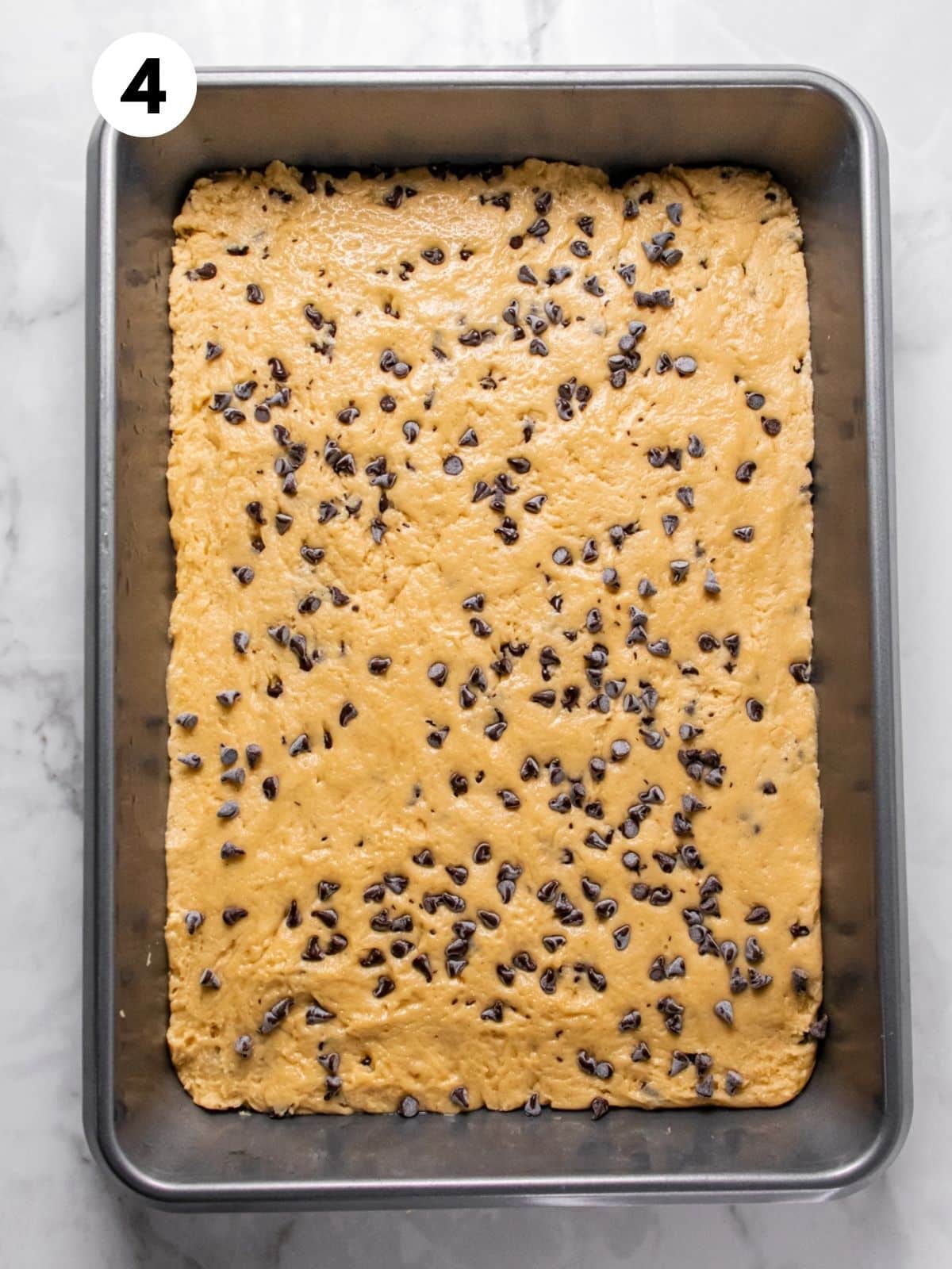 A shallow baking pan containing the mixture for healthy chocolate chip cookie bars, ready for the oven.