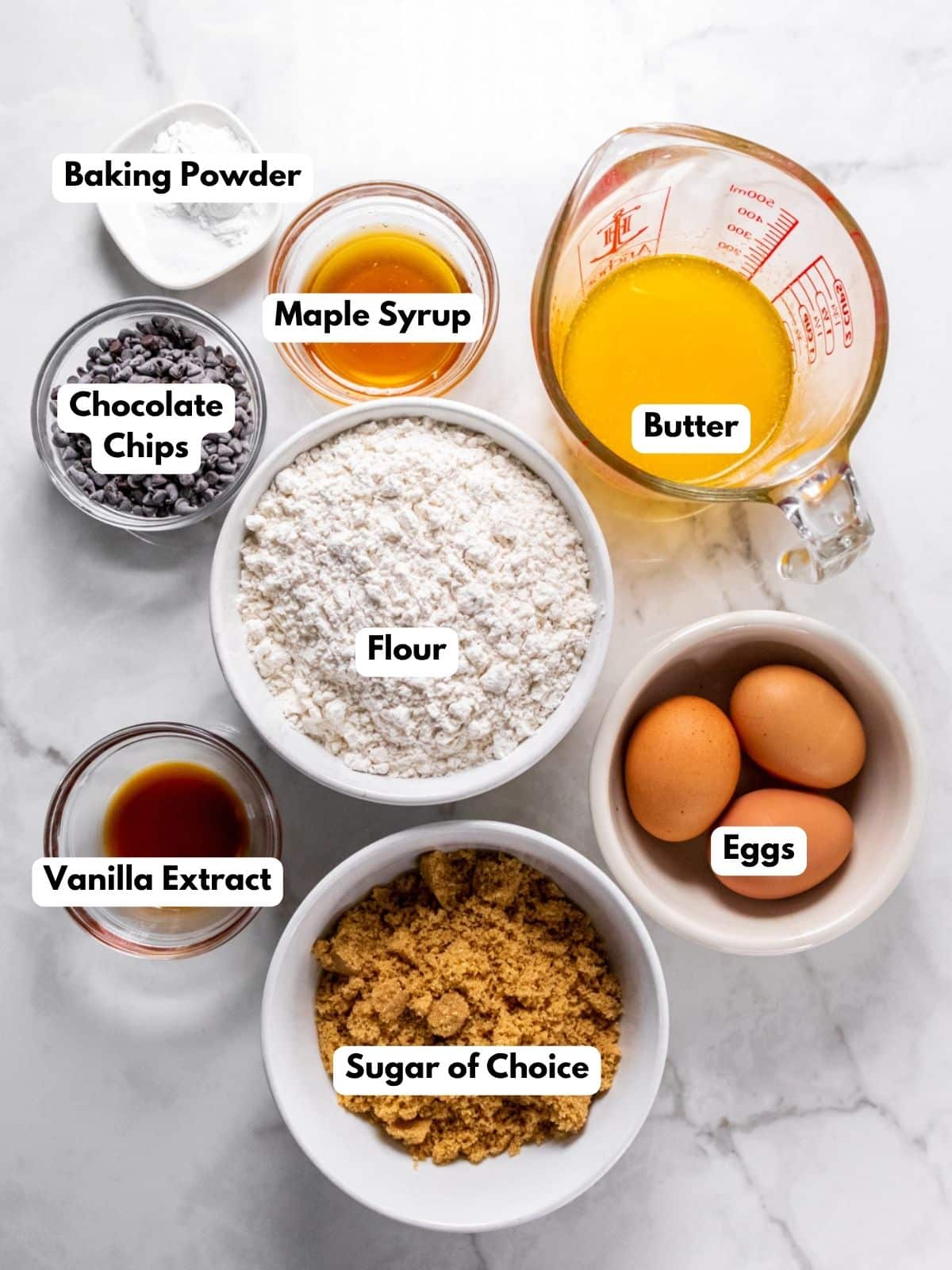 Ingredients for healthy cookie bars labelled, in bowls, on a white marbled countertop.