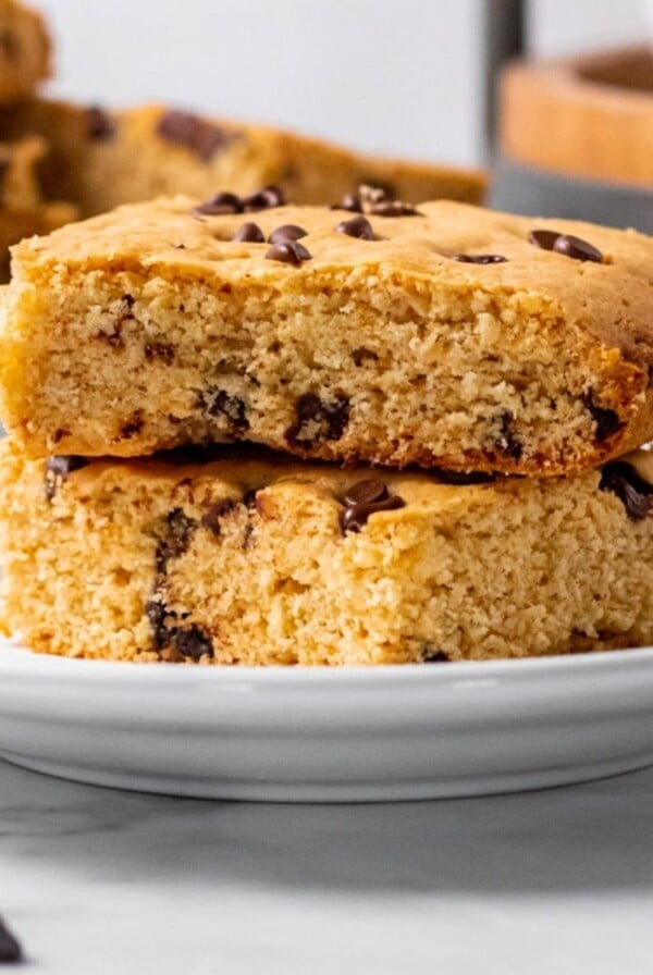 A close up of two slices of healthy cookie bar squares, stacked on top of one another, sitting on a white plate.