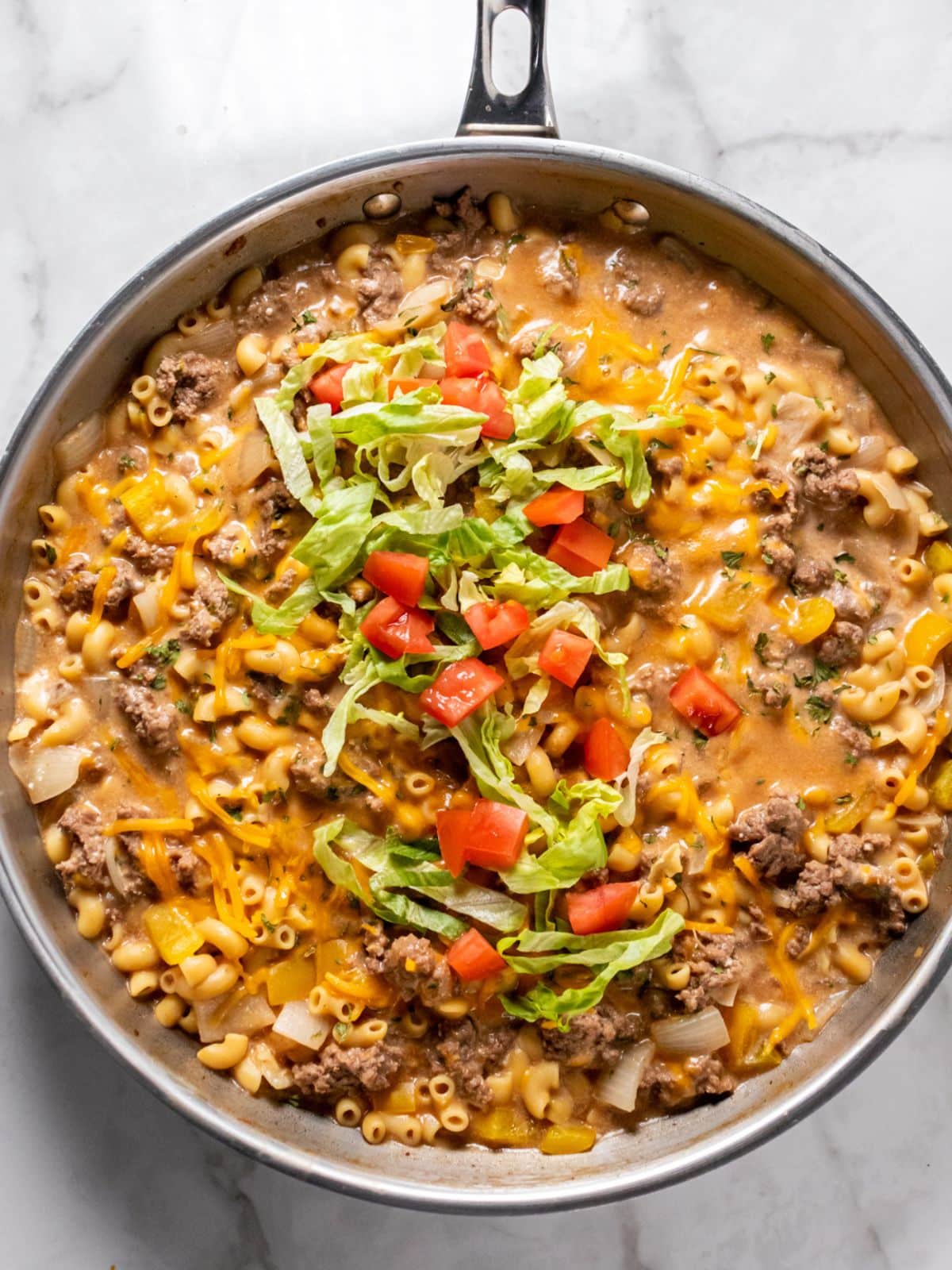 Healthy cheeseburger macaroni skillet on the table topped with lettuce and tomatoes.