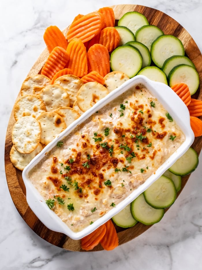 white casserole dish with dip on a board with vegetables and chips