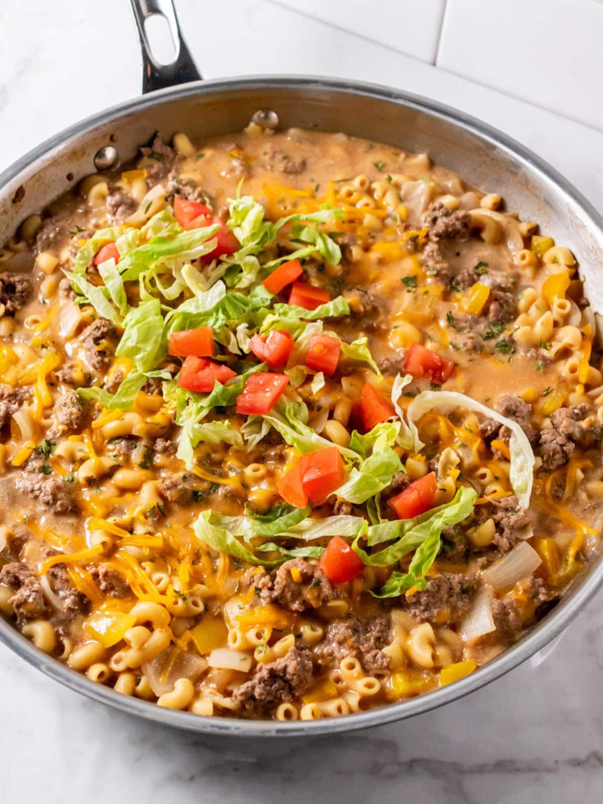 A cheeseburger macaroni skillet on the table with lettuce and tomato on top.