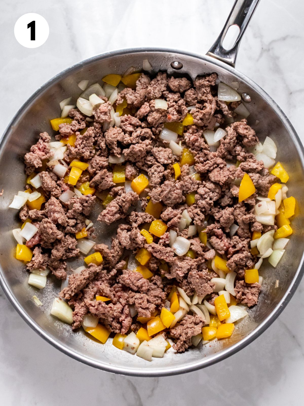 Ground beef, onions, and bell pepper cooked in a skillet.