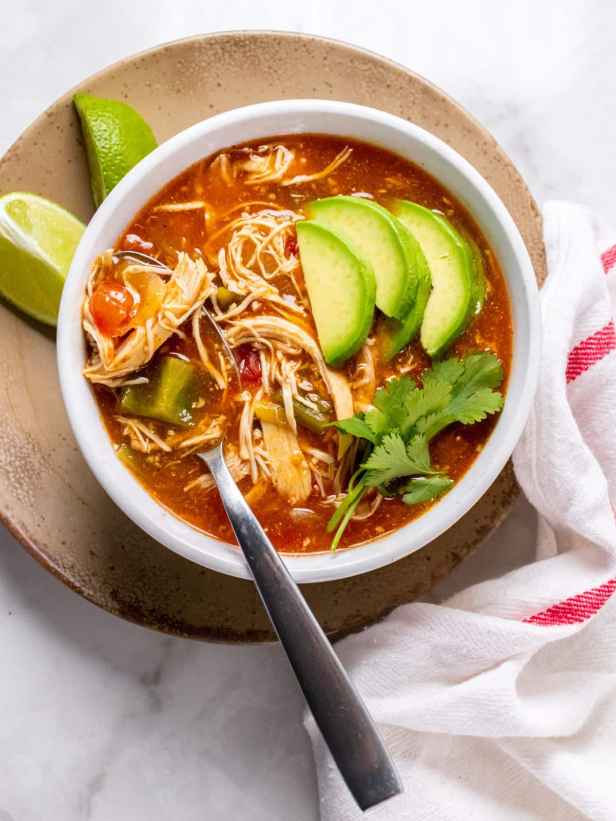 A bowl of chicken enchilada soup on the table with a spoon in the bowl.