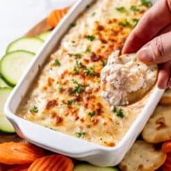 A hand scooping up a bite of shrimp dip with a cracker.