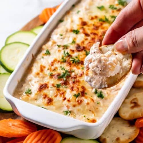 A hand scooping up a bite of shrimp dip with a cracker.