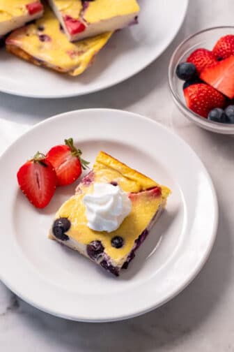 white plate with strawberries and slice of baked good with whipped cream
