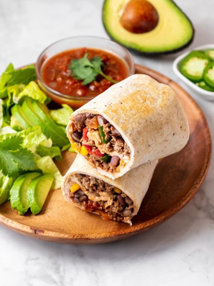2 burrito wraps on a brown plate with sliced avocado and salsa