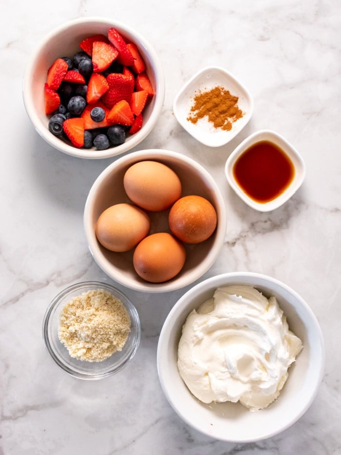 white bowls on a marble counter with eggs, berries, flour and yogurt