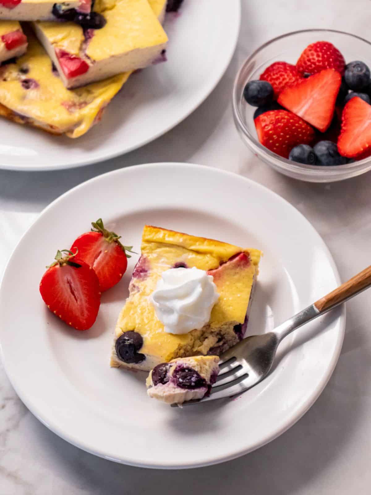 egg bake on a white plate with a fork and sliced strawberries