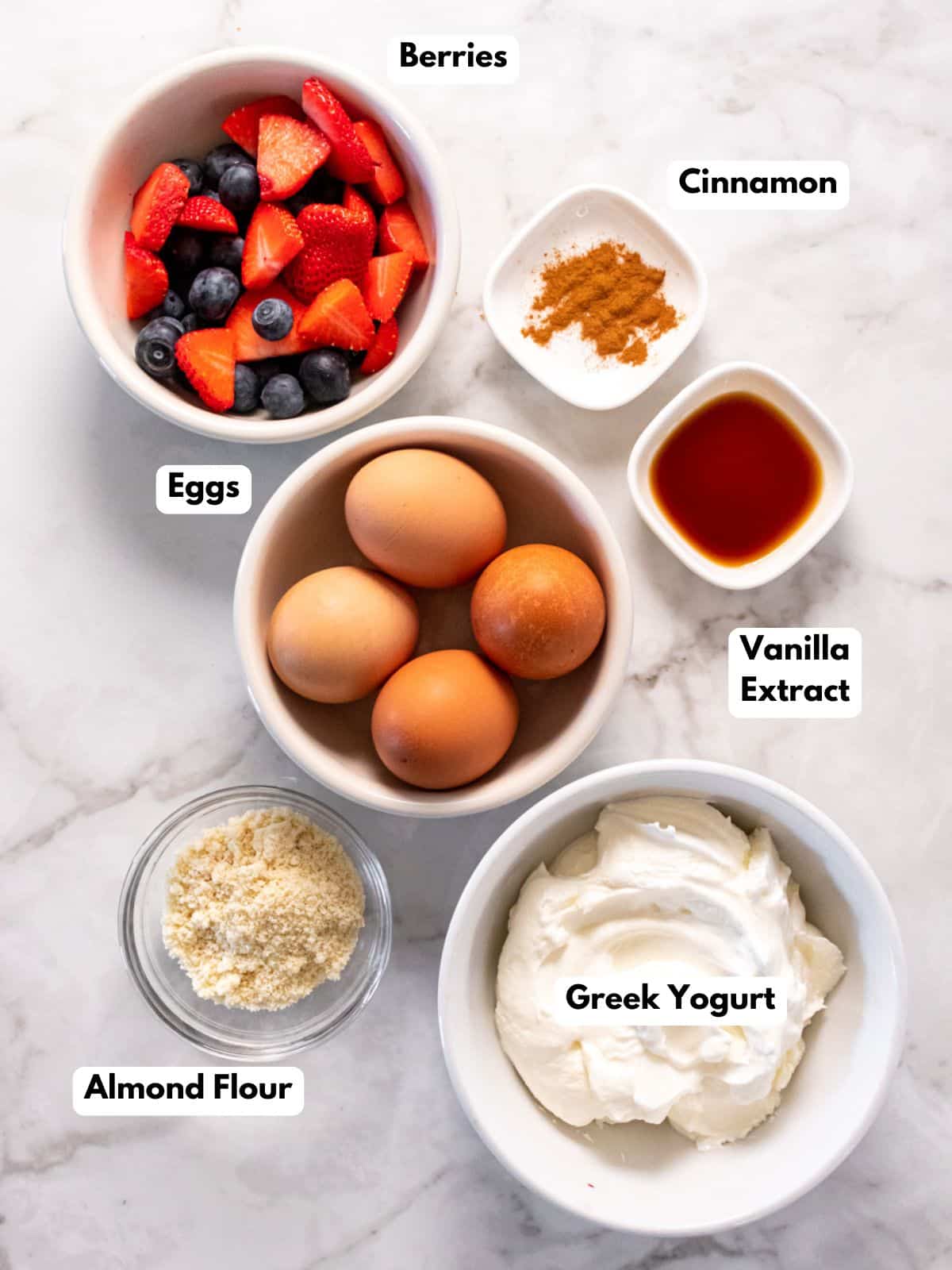 white bowls on a marble counter with eggs, berries, flour and yogurt