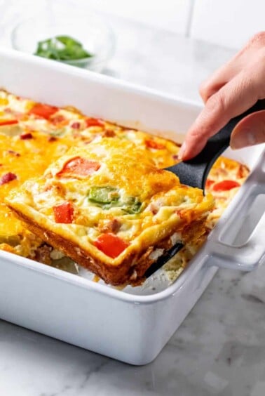 A spatula lifting up a serving of omelette casserole from the dish.