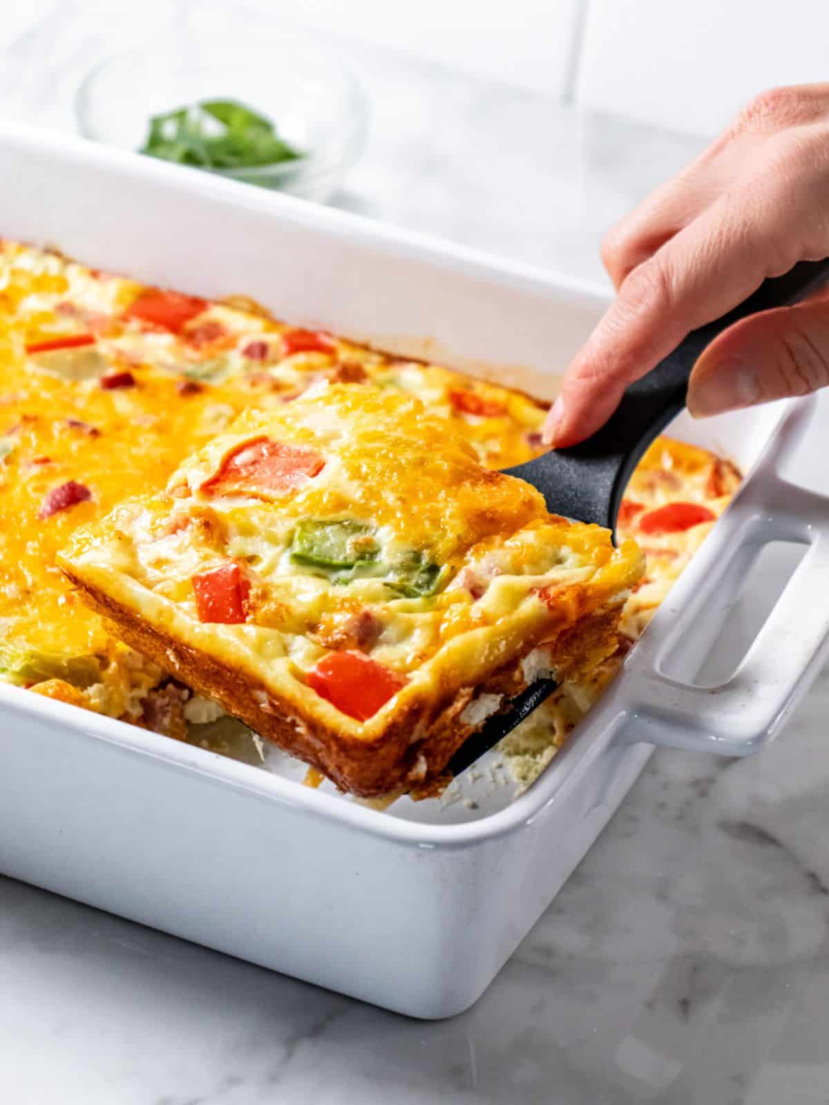 A spatula lifting up a serving of omelette casserole from the dish.
