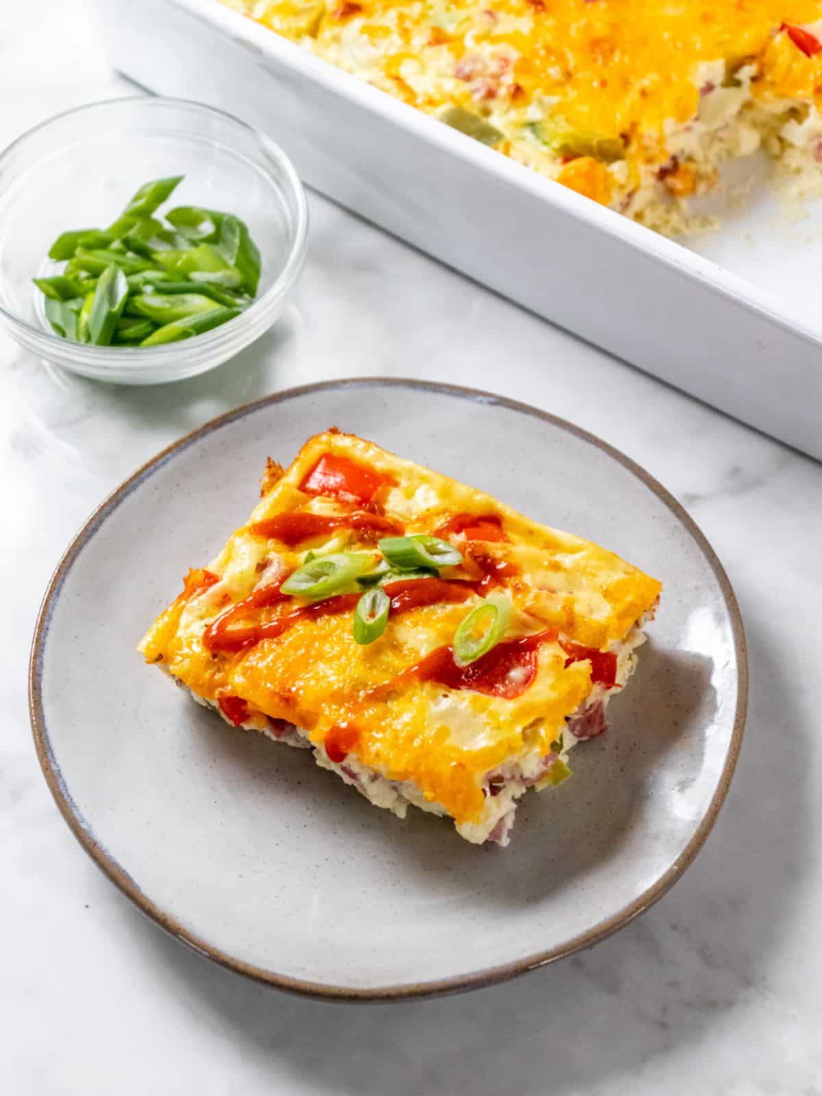A slice of Denver omelet on a silver plate with more in a casserole dish in the background.