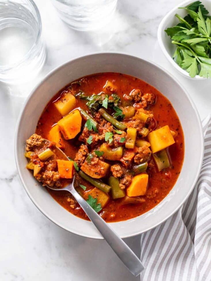 A bowl of healthy hamburger soup on the table with a spoon resting in the bowl.