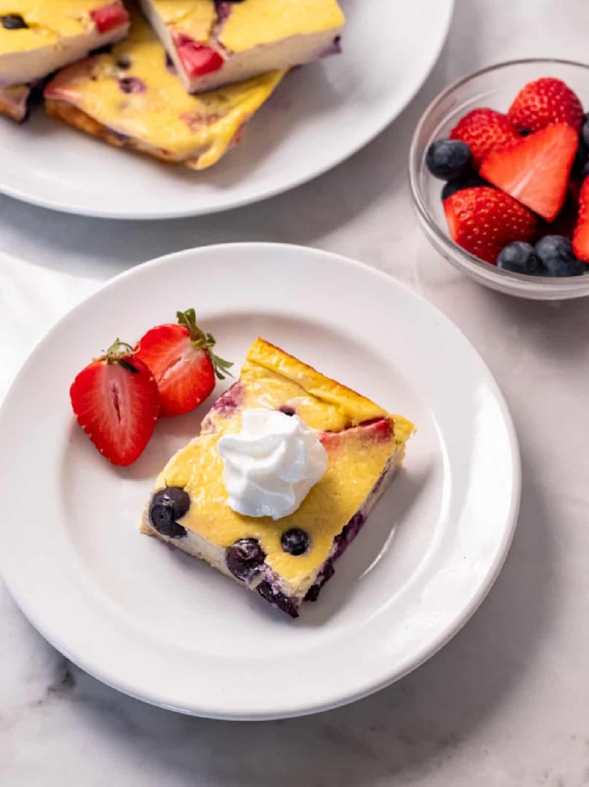 slice of yogurt cake on a white plate with whipped cream on top and two sliced strawberries.