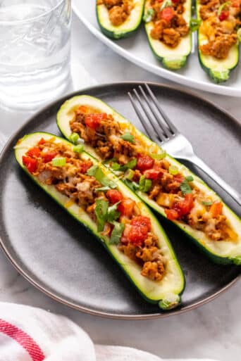 two zucchini boats stuffed with ground turkey on a brown plate with a fork