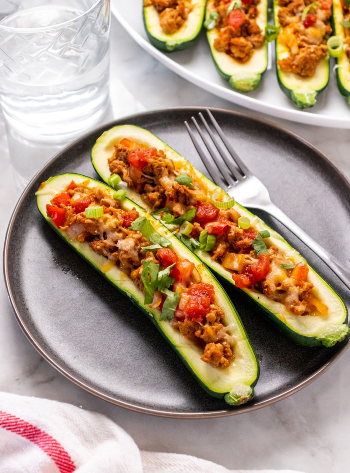 two zucchini boats stuffed with ground turkey on a brown plate with a fork