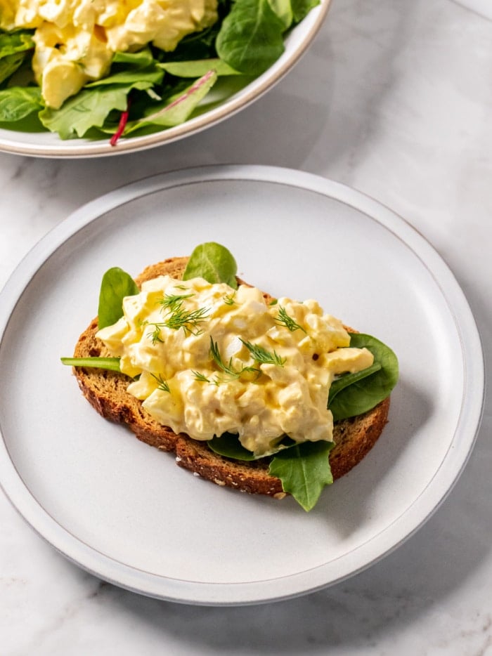 egg salad on a slice of toast with spinach on a white plate