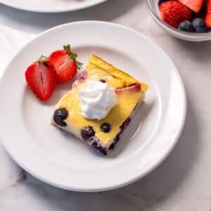 A slice of baked yogurt on a plate garnished with whipped cream and berries.