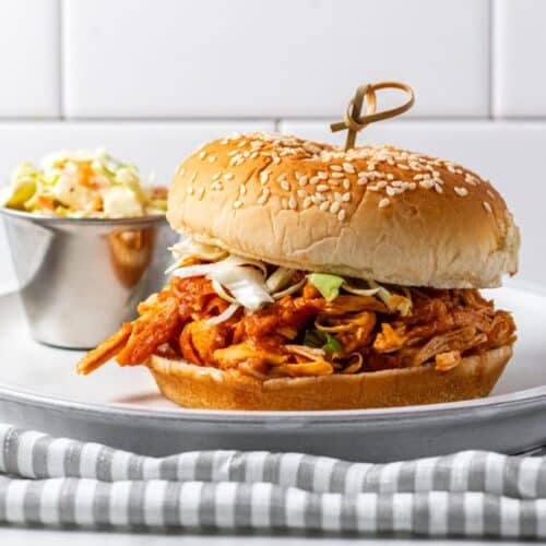 Chicken sloppy joe on a plate with ramekin of slaw to the side.