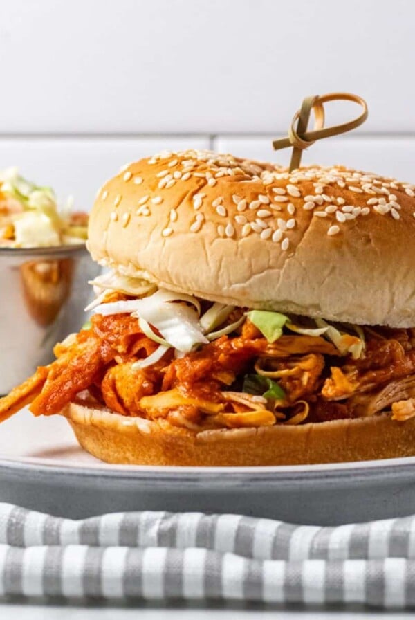 Chicken sloppy joe on a plate with ramekin of slaw to the side.
