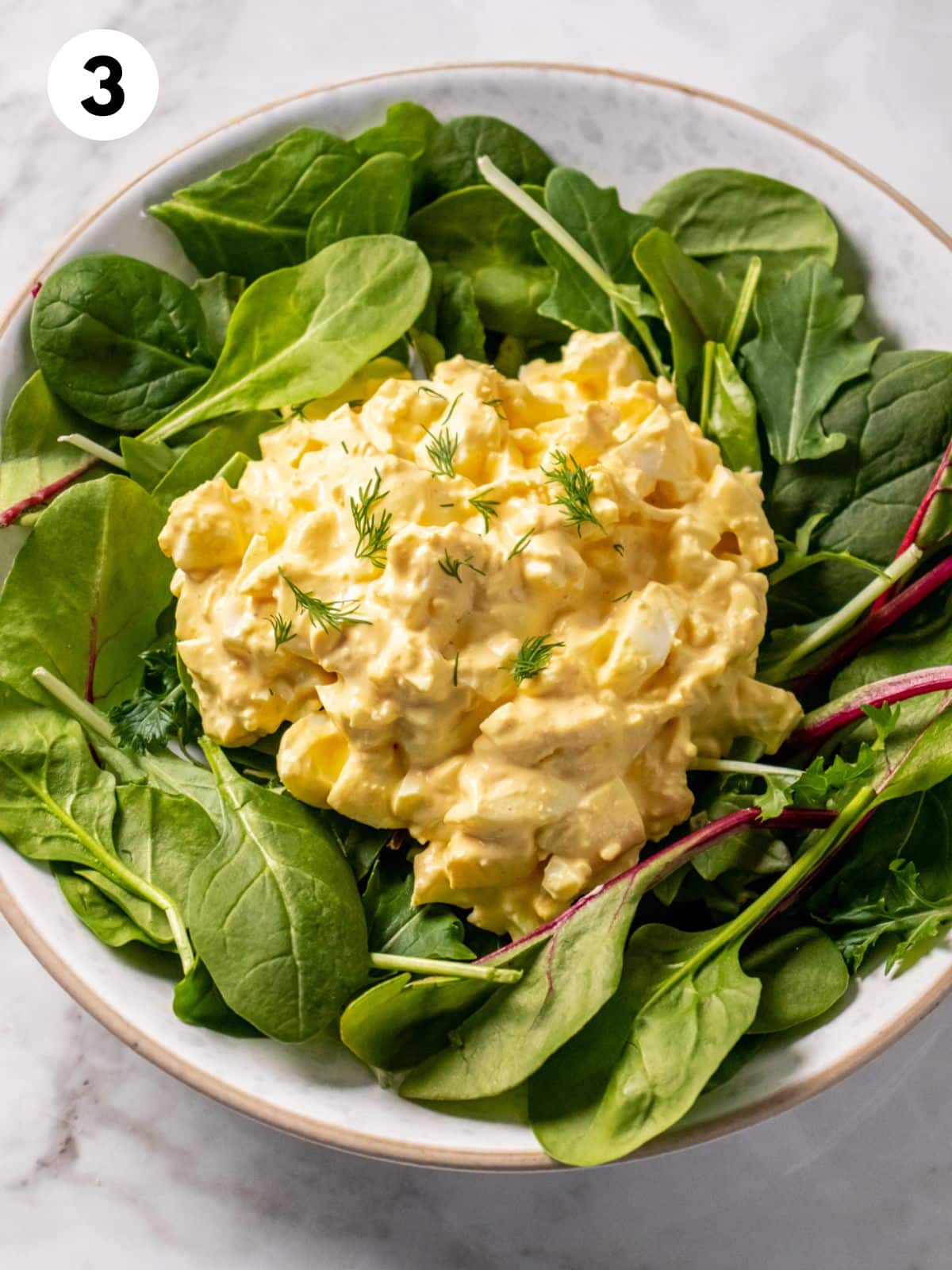 High protein egg salad on a bed of greens in a bowl.