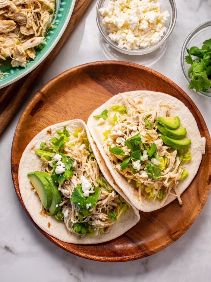 two open tacos with shredded chicken, avocado and cilantro on a brown plate