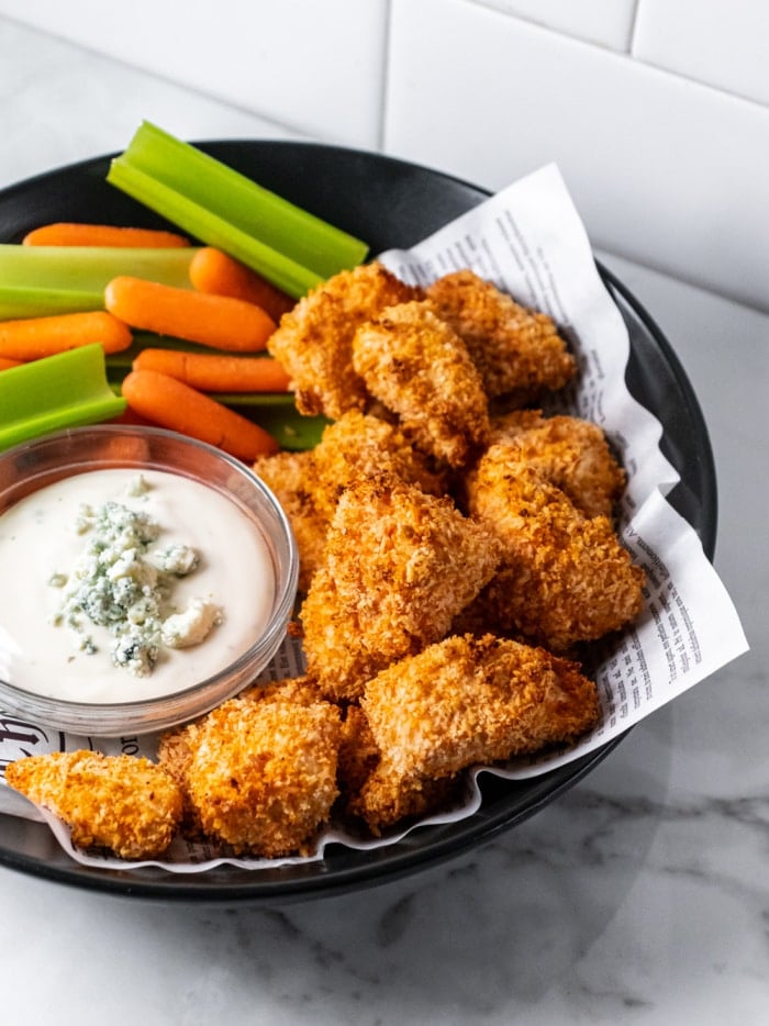 chicken nuggets in a black bowl with dipping sauce and veggies