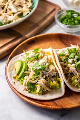 two tacos with shredded chicken on a brown plate