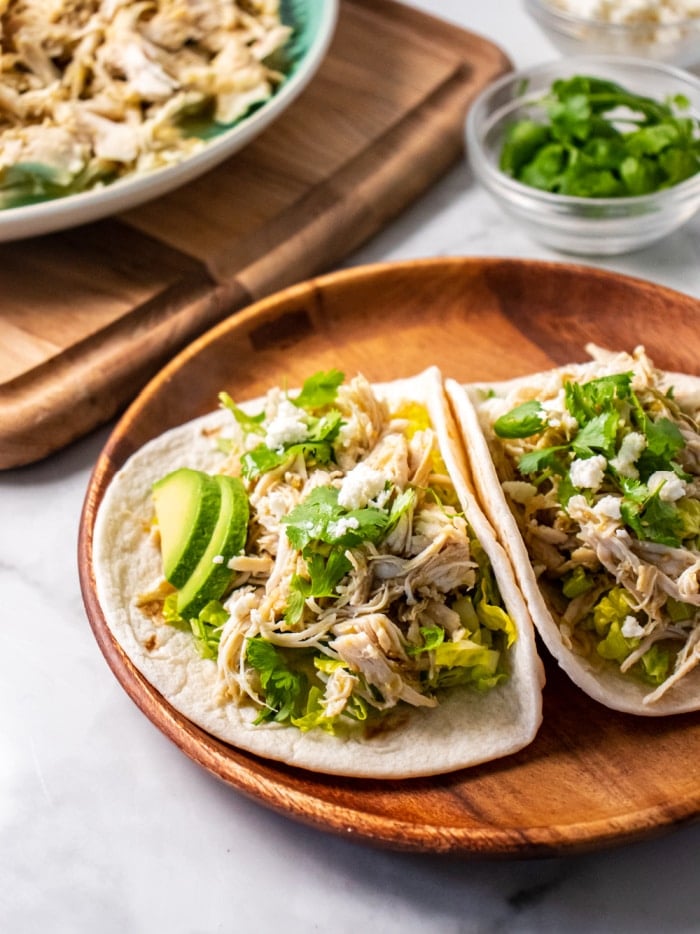 two tacos with shredded chicken on a brown plate.