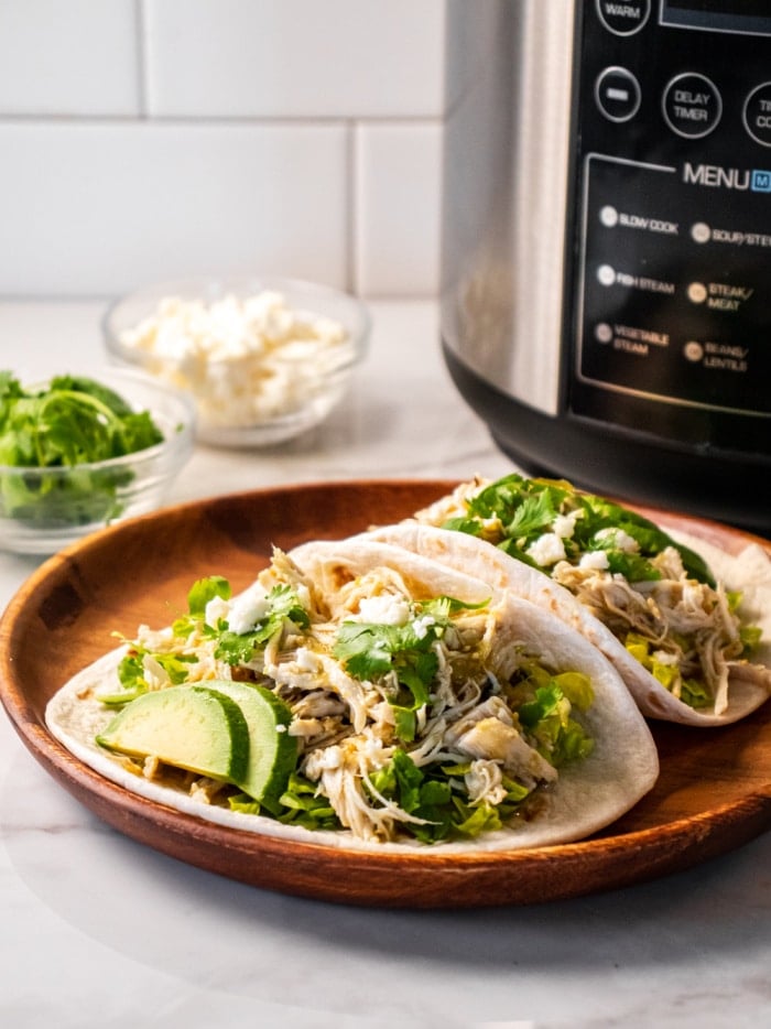 two tacos on a brown plate with an instant pot behind it