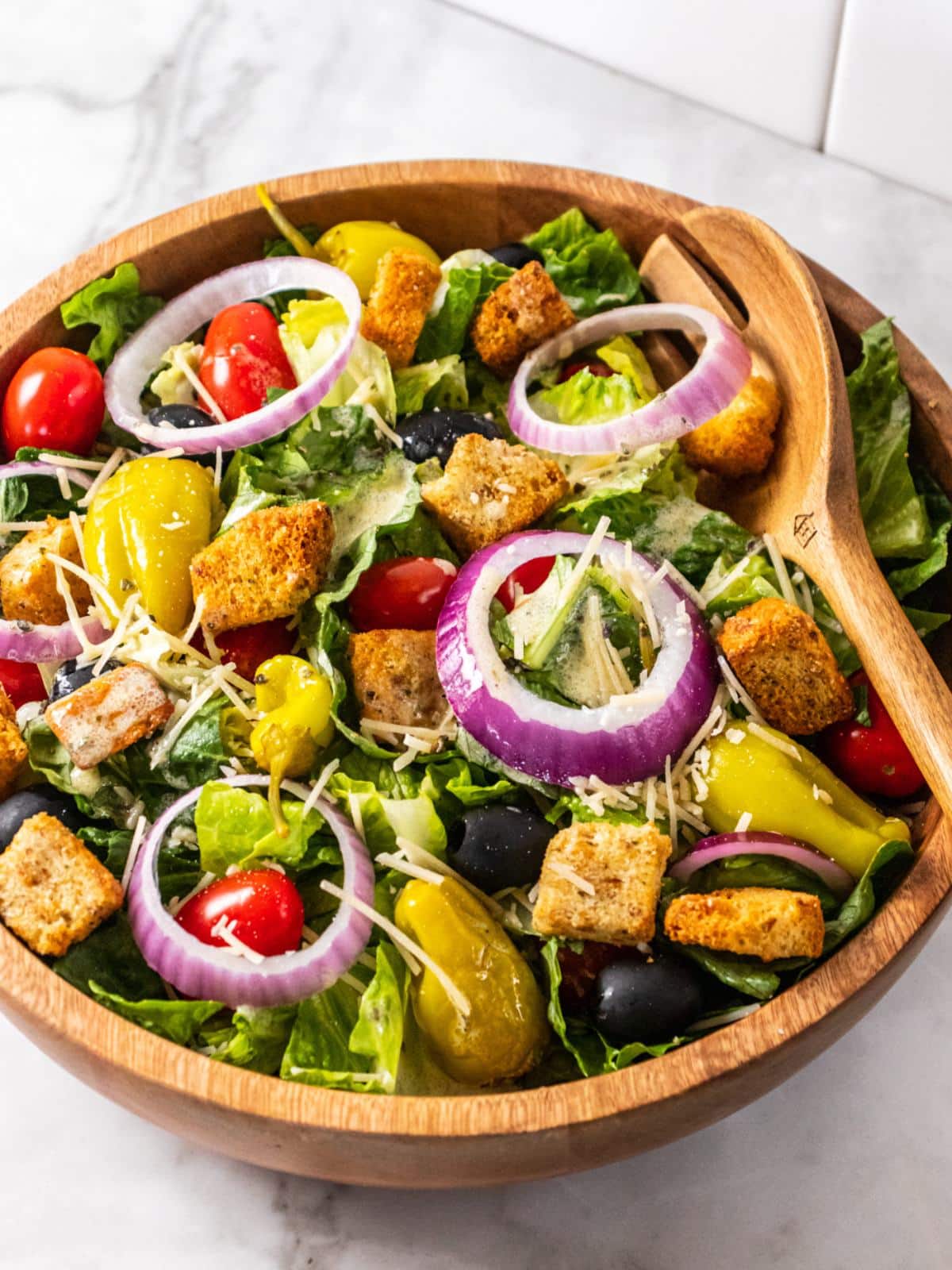 A wooden salad bowl with a copycat Olive Garden salad on a white counter.