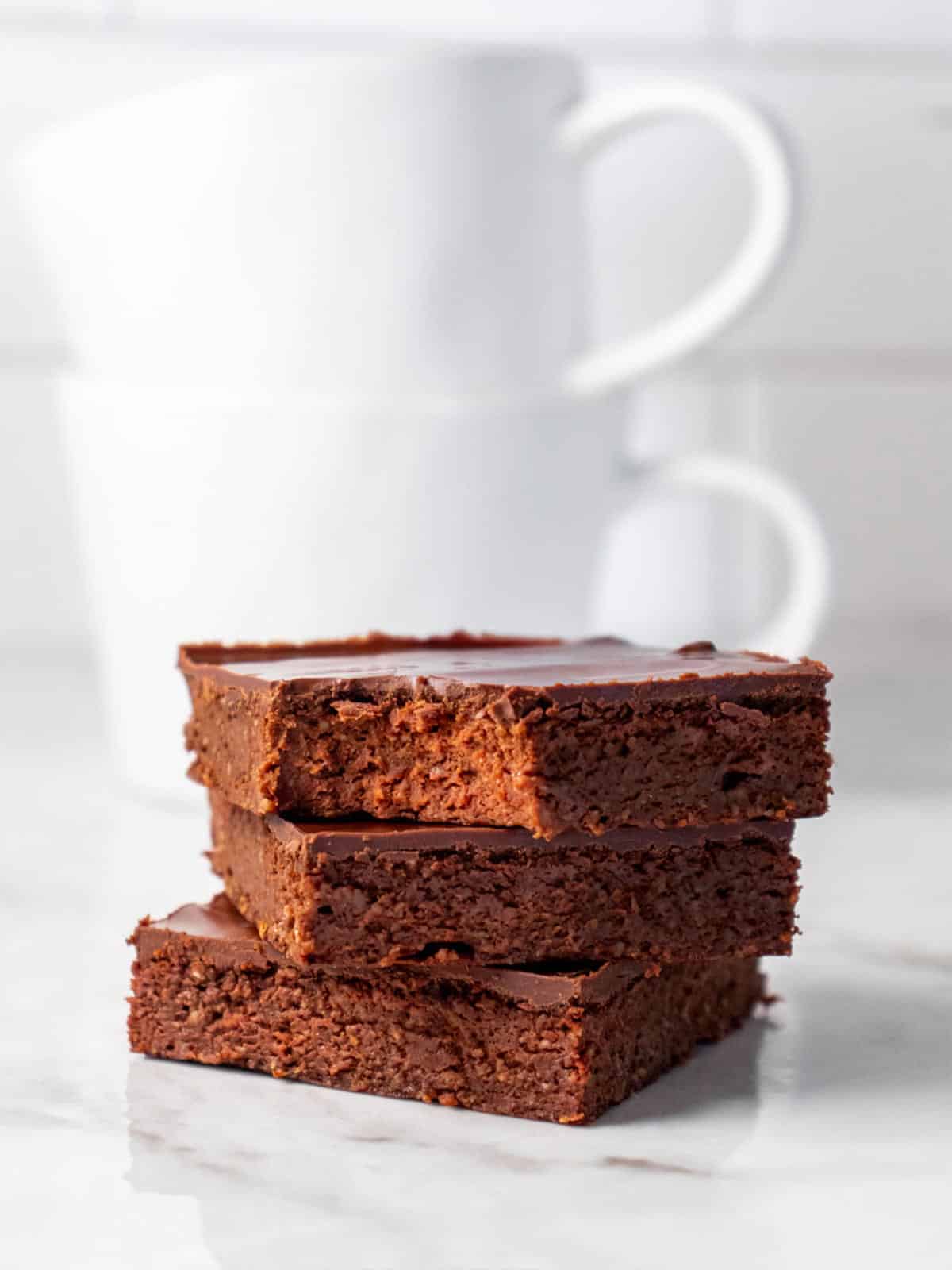 Three brownies stacked on top of each other with a bite missing from the one on top.