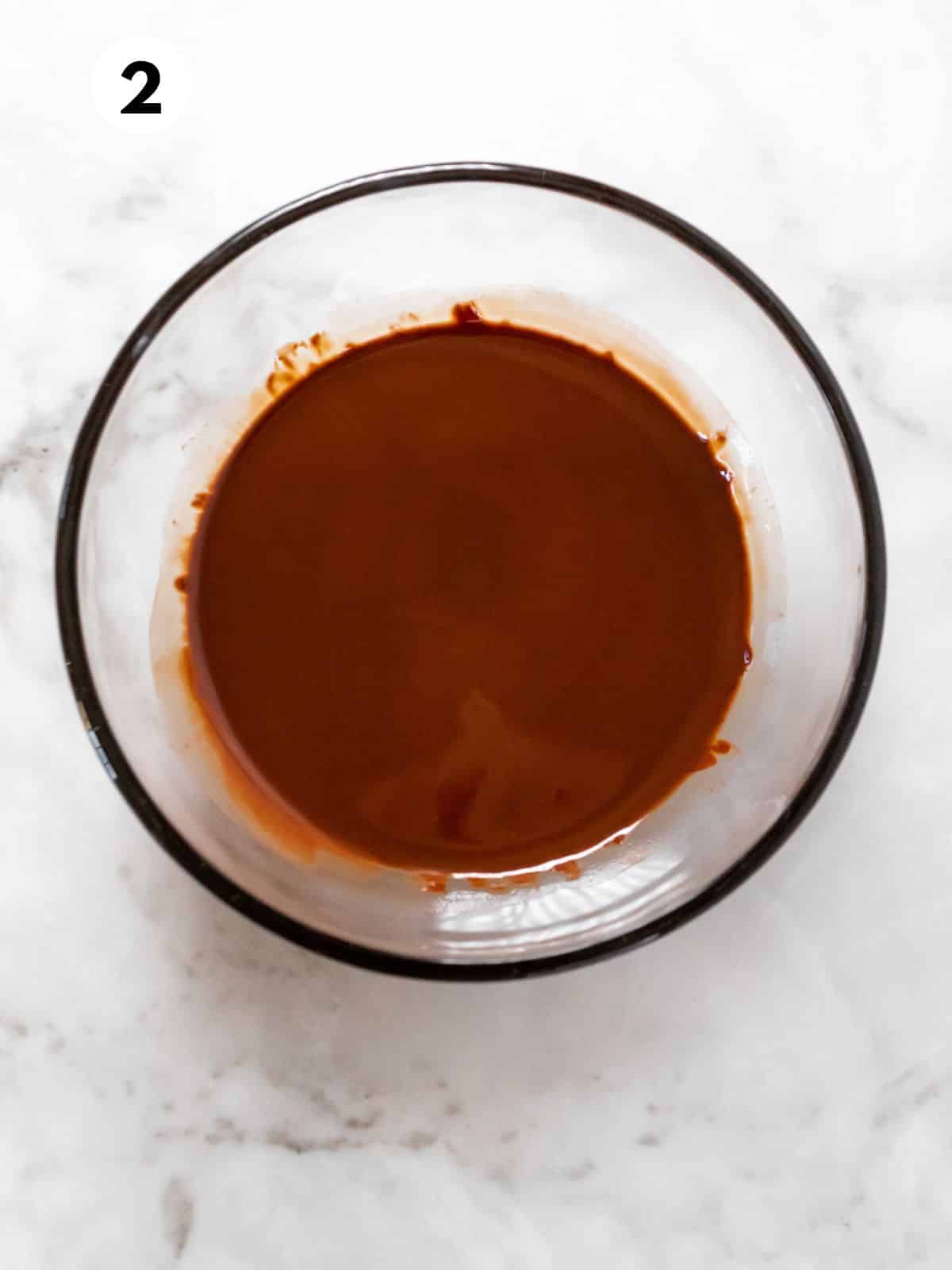 Melted chocolate and olive oil in a glass mixing bowl.