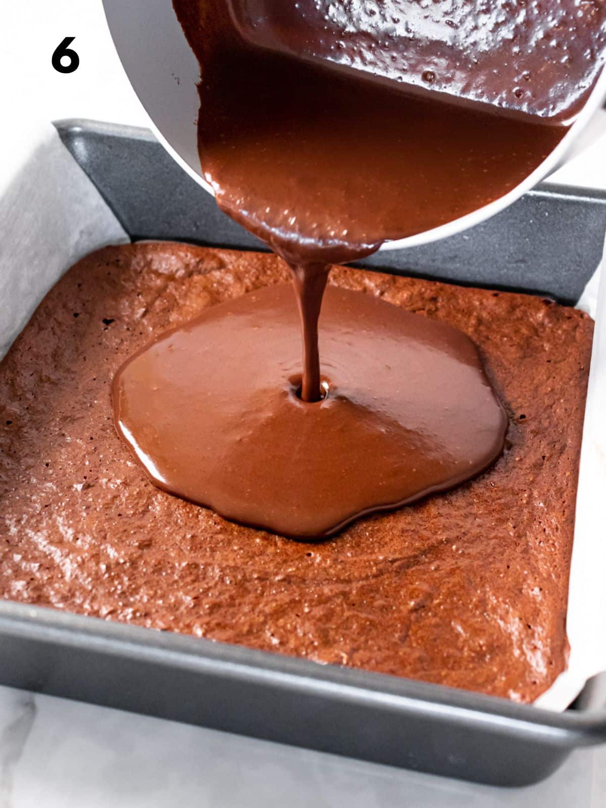 Pouring the chocolate ganache over a pan of baked greek yogurt brownies.