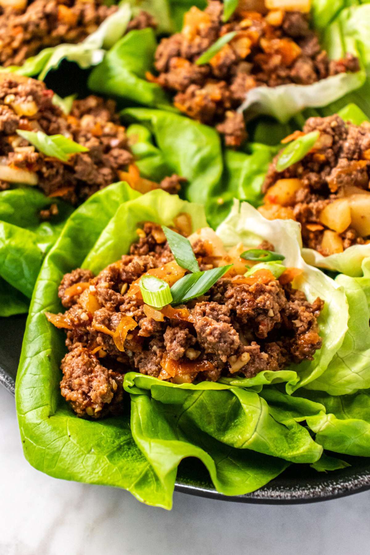A lettuce wraps ground beef in it and green onions on top.
