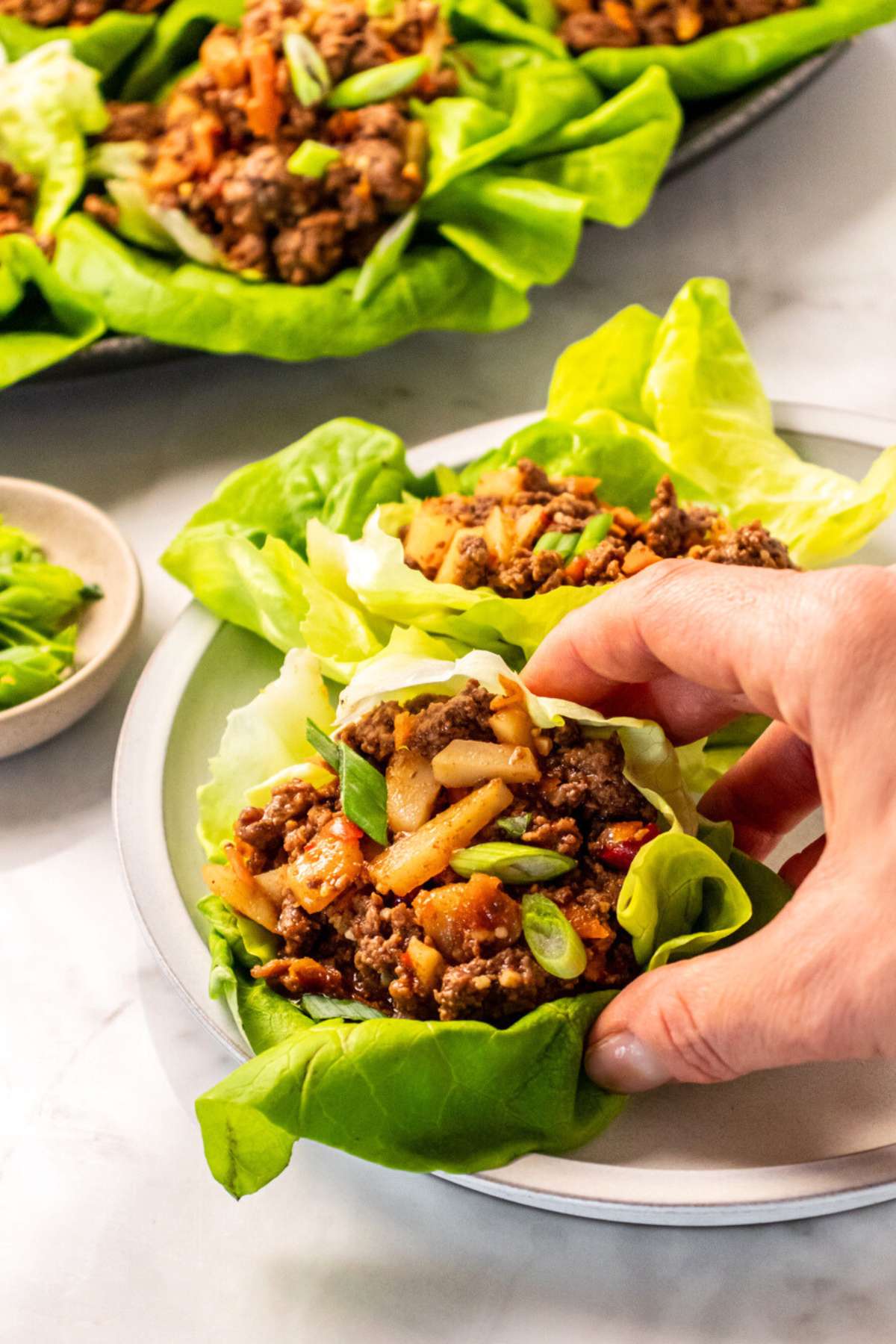 A hand picking up a lettuce wrap with ground beef on a plate.