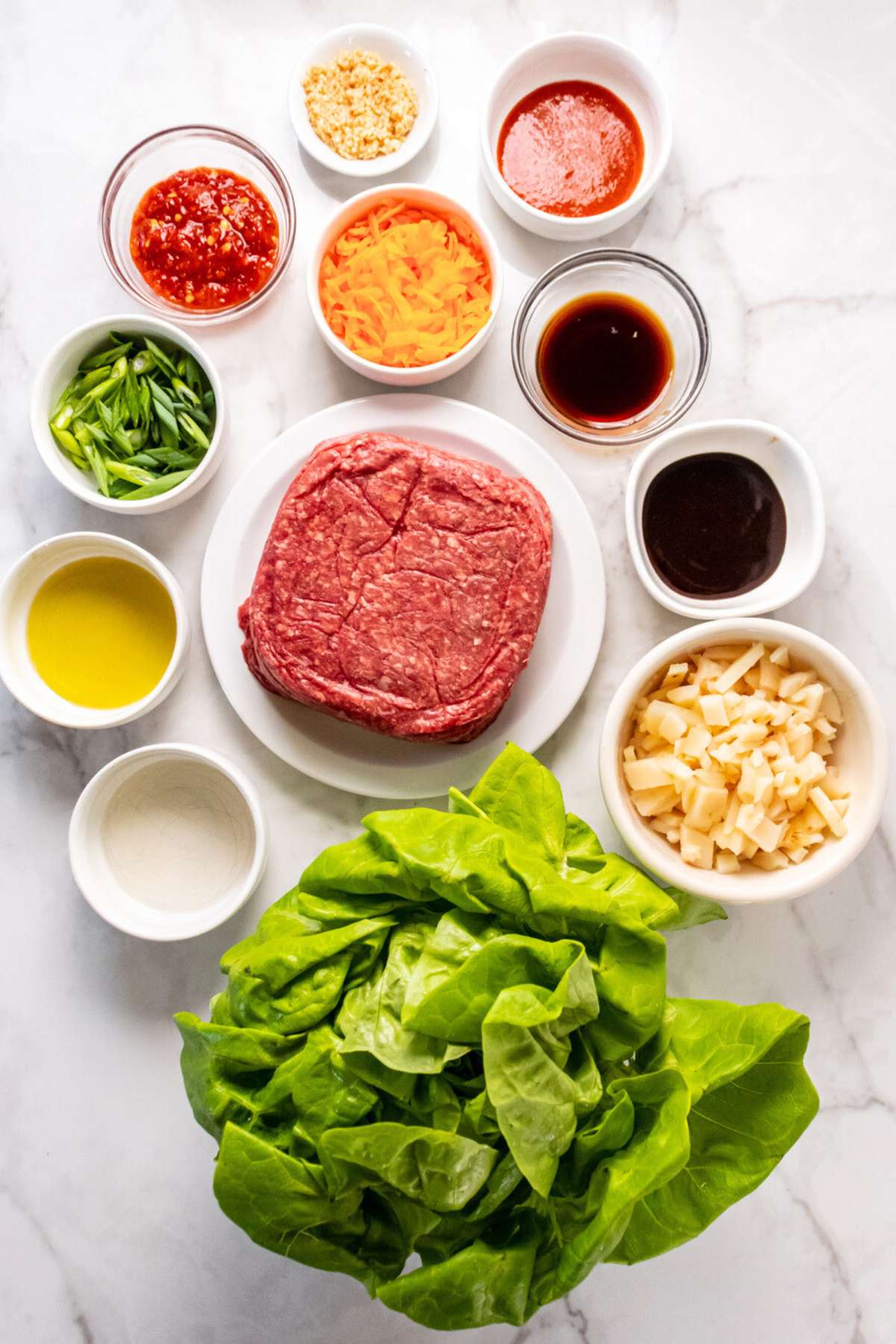 Ingredients in bowls with ground beef on a white plate to make ground beef lettuce wraps.
