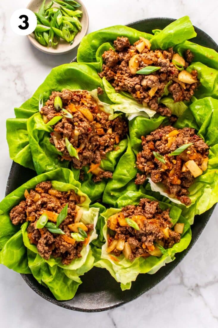 Ground beef lettuce wraps on a platter with green onions in a little bowl.