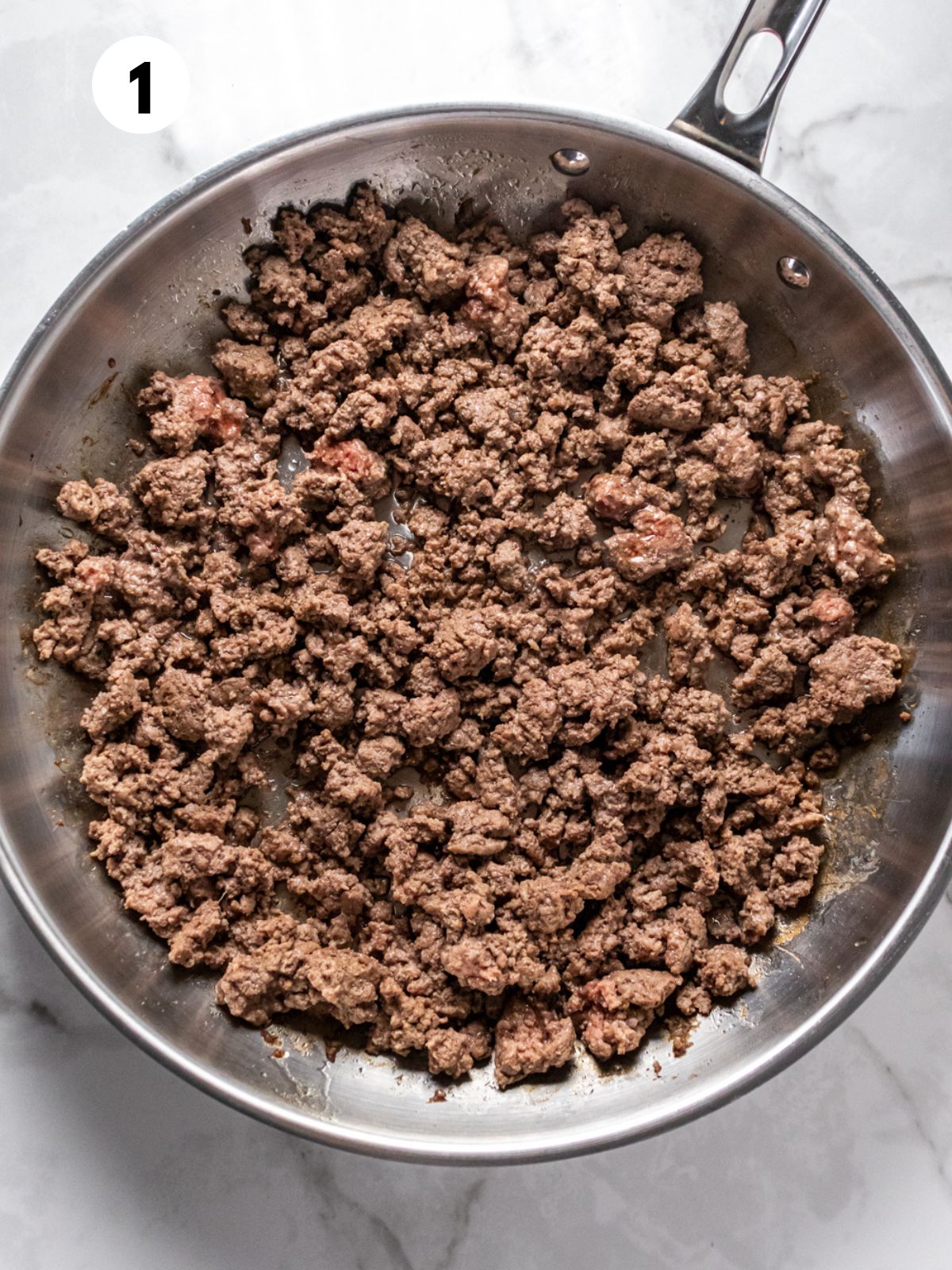 Ground beef partially cooked in a skillet.