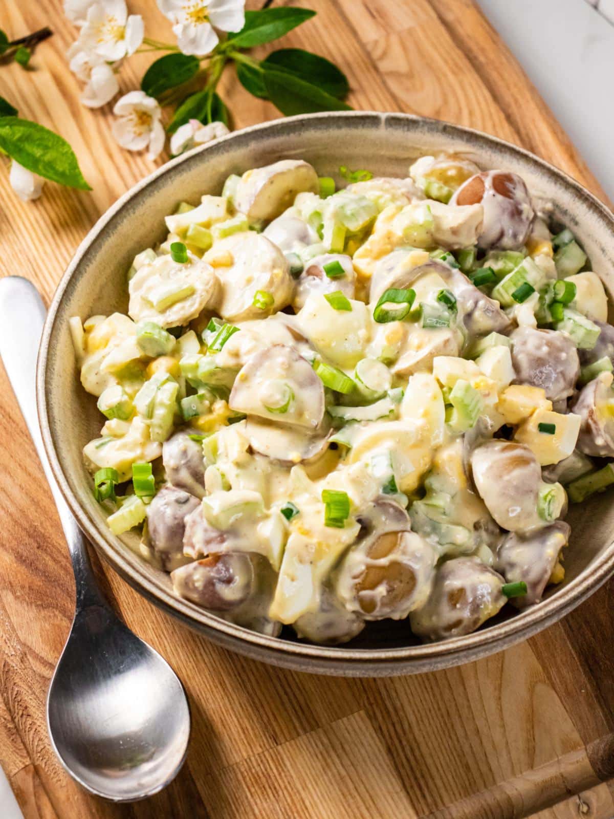 Healthy potato salad in a tan bowl on a wooden board.