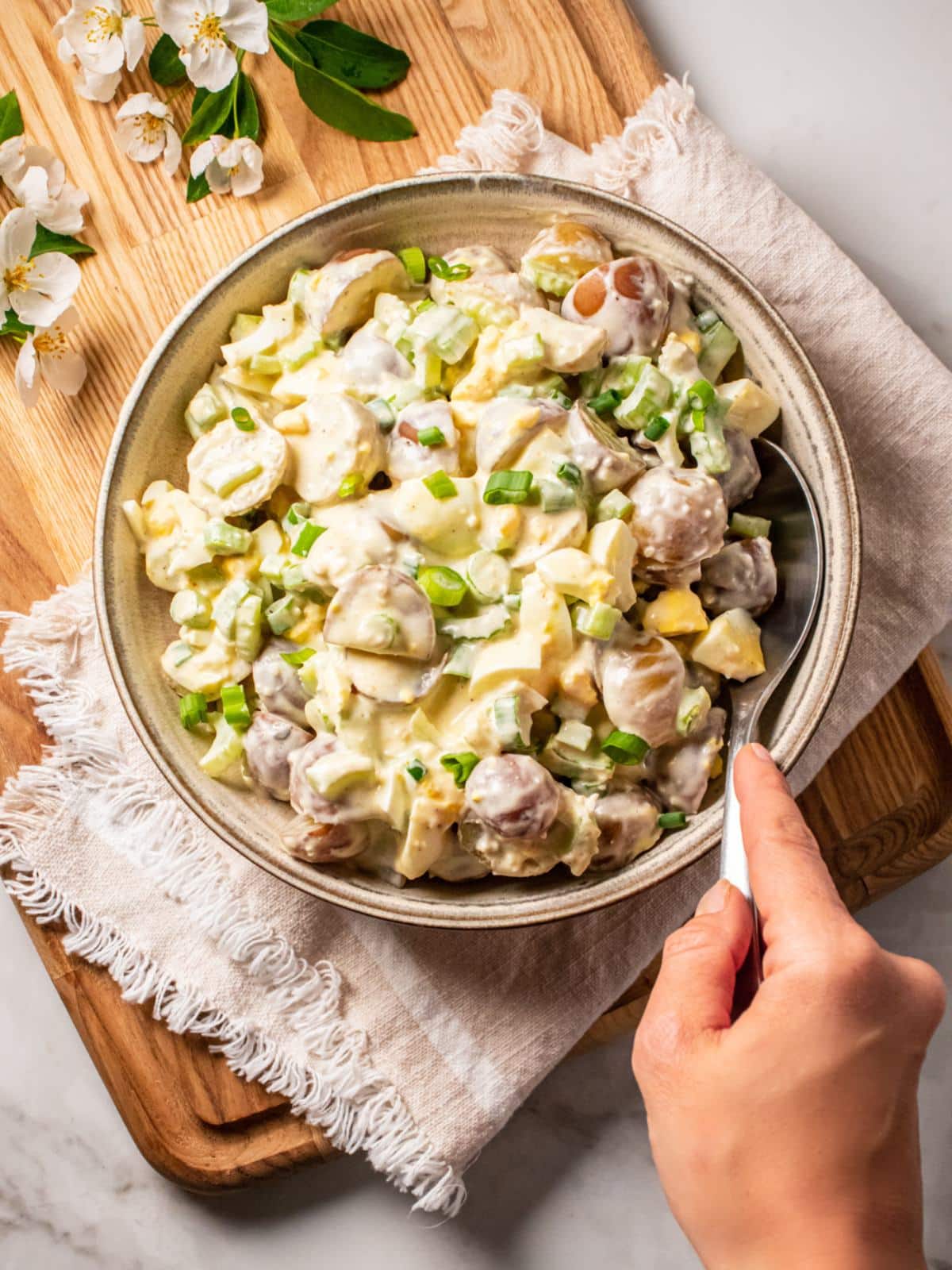 A bowl of healthy potato salad on a table with a hand on a spoon to scoop.