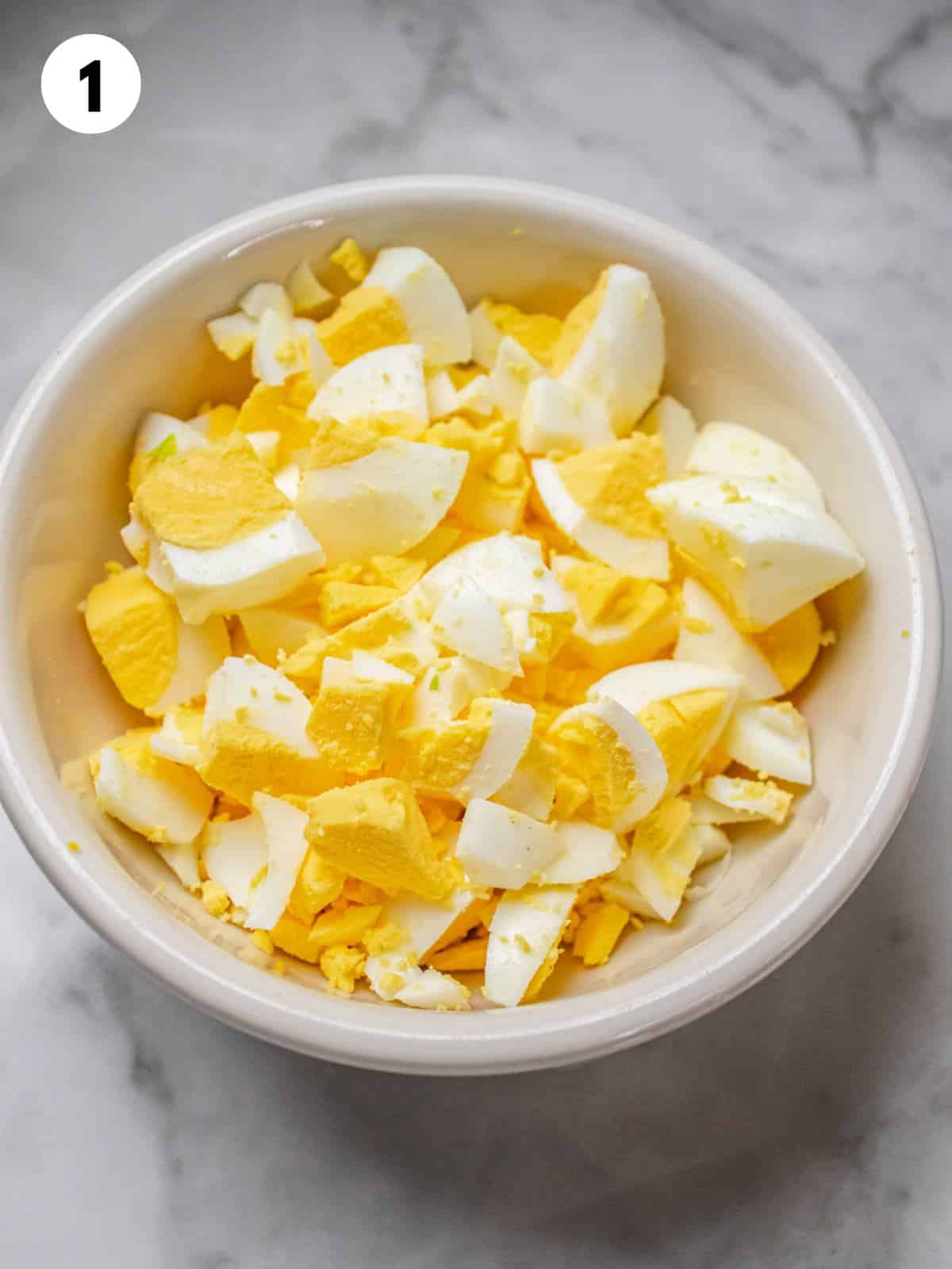 Hard boiled eggs chopped in a white bowl.