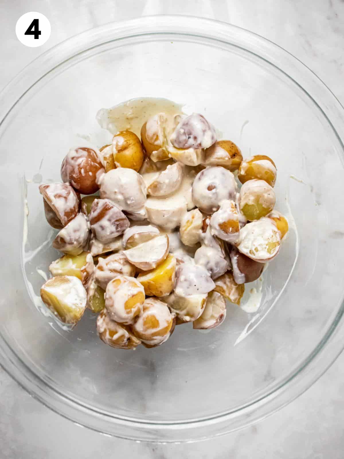 Potatoes sliced in a clear mixing bowl with potato salad dressing.