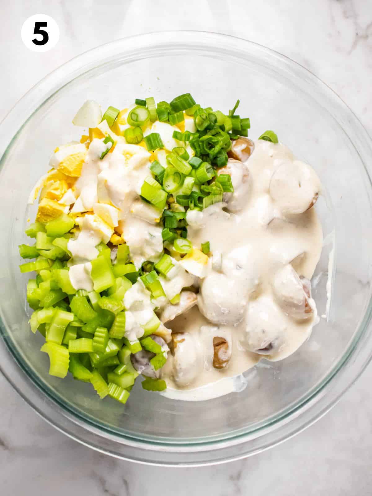 Potato salad ingredients in a mixing bowl with yogurt dressing.