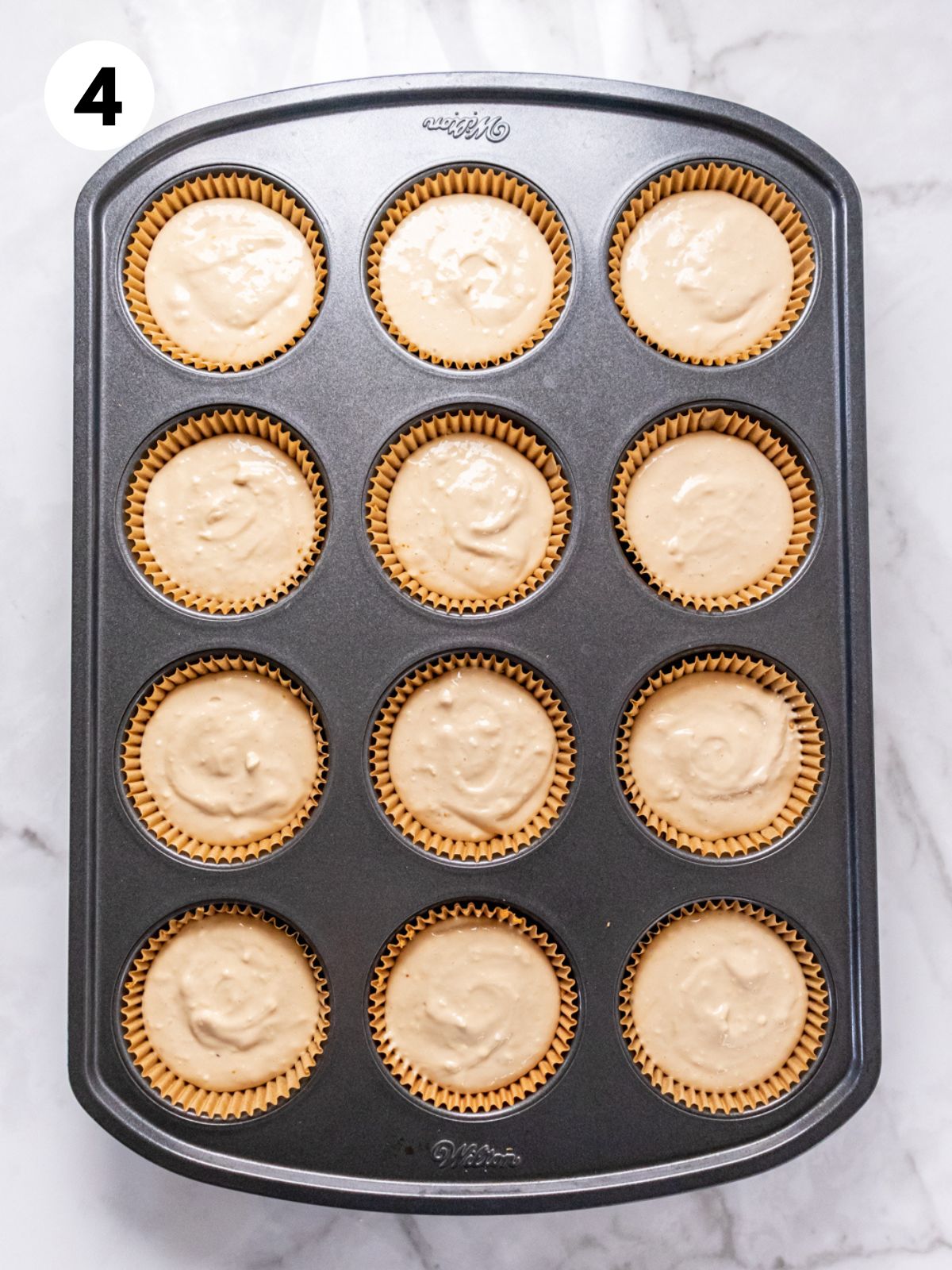 Healthy cheesecake batter poured on top of the crust in a muffin pan.