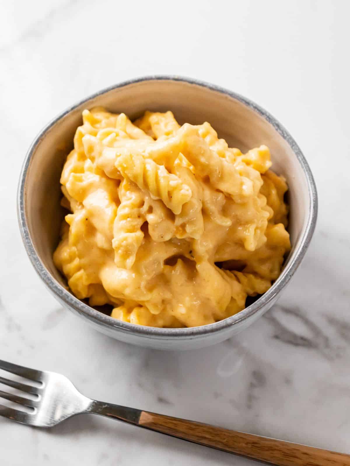 A bowl of healthy mac and cheese on the table with a fork next to the bowl.