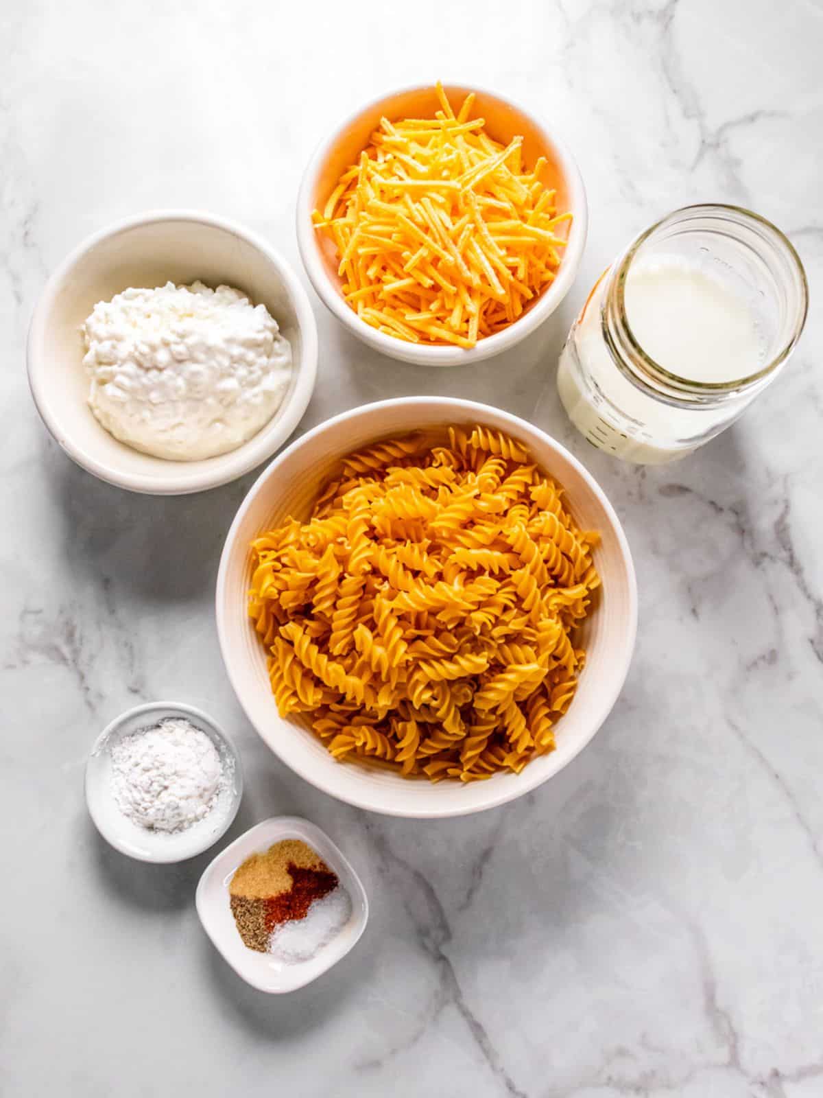 Ingredients to make cottage cheese mac and cheese on the table in white bowls.